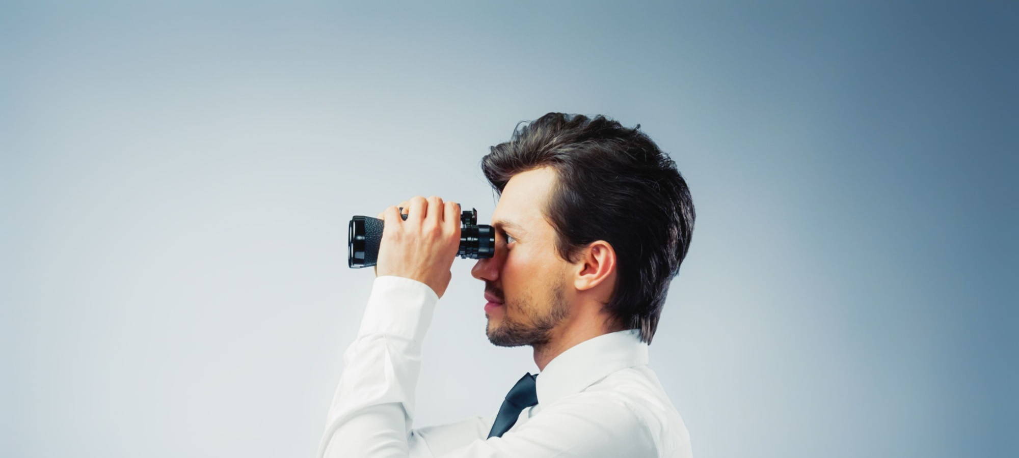 A man looks through a pair of binoculars, searching for a new opportunity